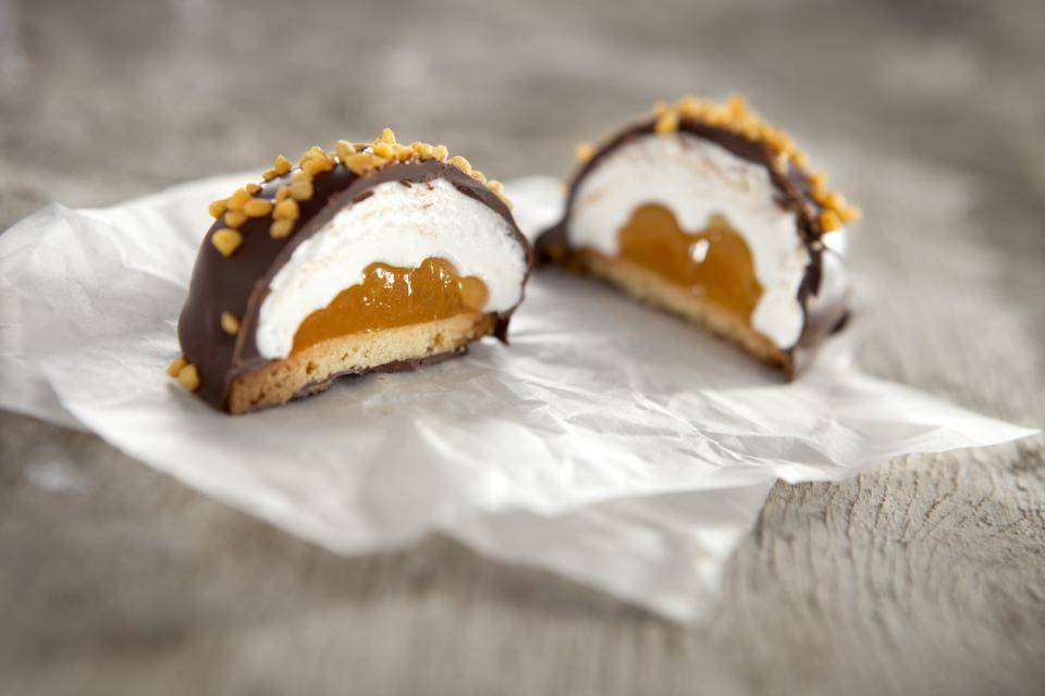 A "snowball" style chocolate-coated round marshmallow is cut in half to reveal an orange fruit filling and cookie base