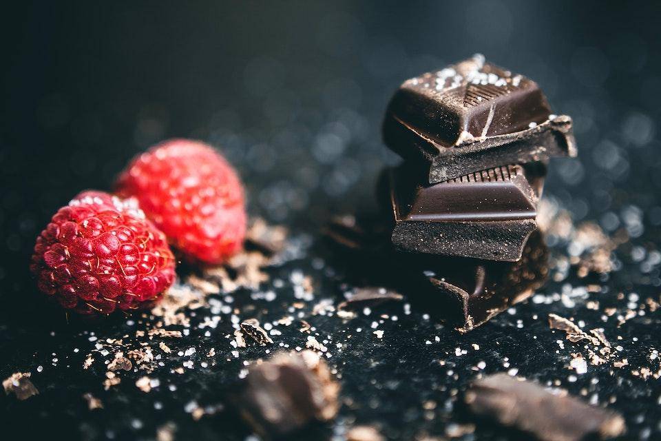 A stack of dark chocolate squares next to raspberries