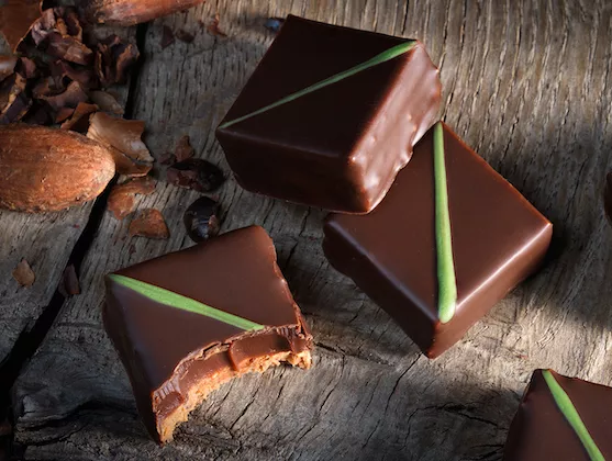 Dark Chocolate Enrobed bonbons decorated with green stripe, of the 3 bonbons, one has had a bite taken out of it